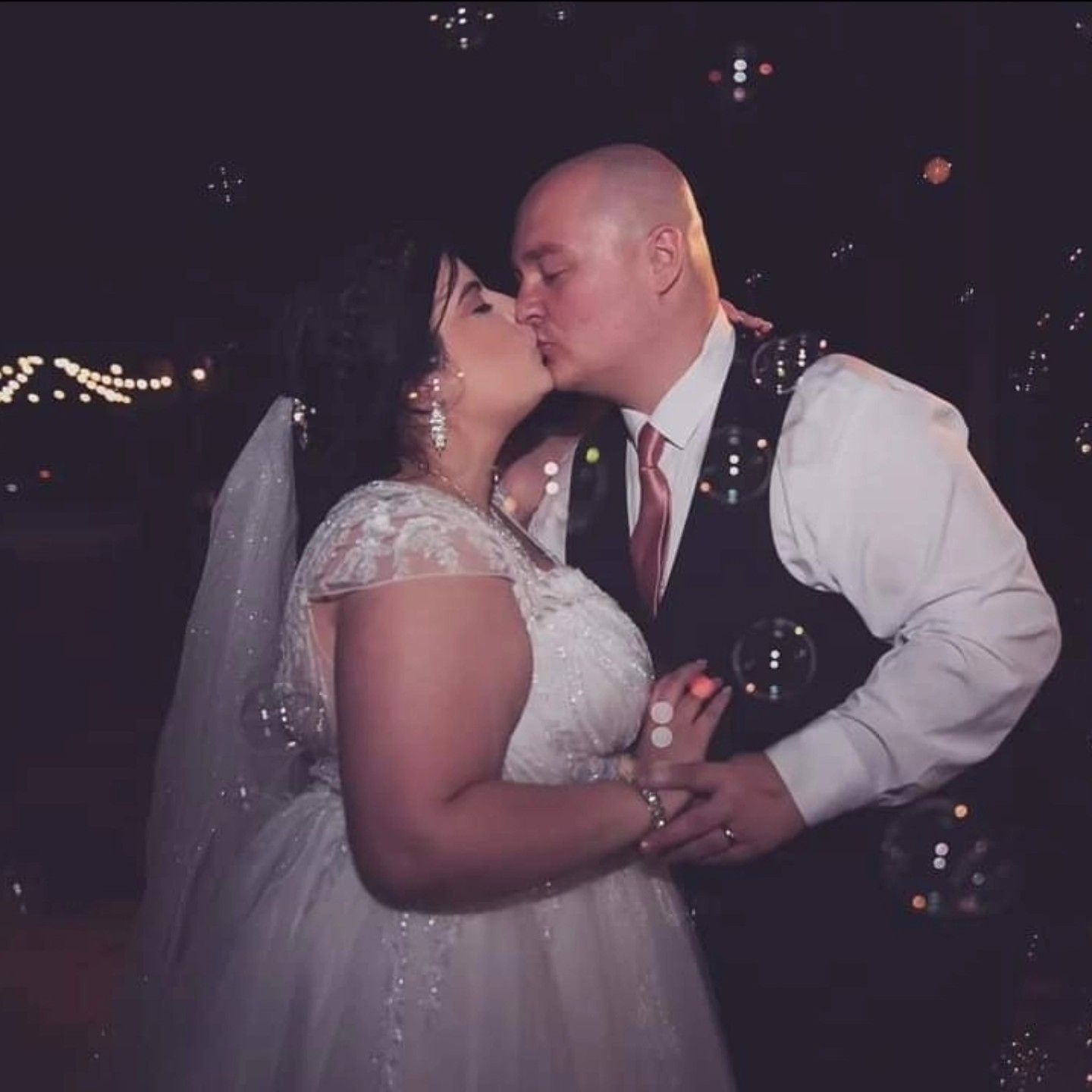 A bride and groom kissing with bubbles in the background.
