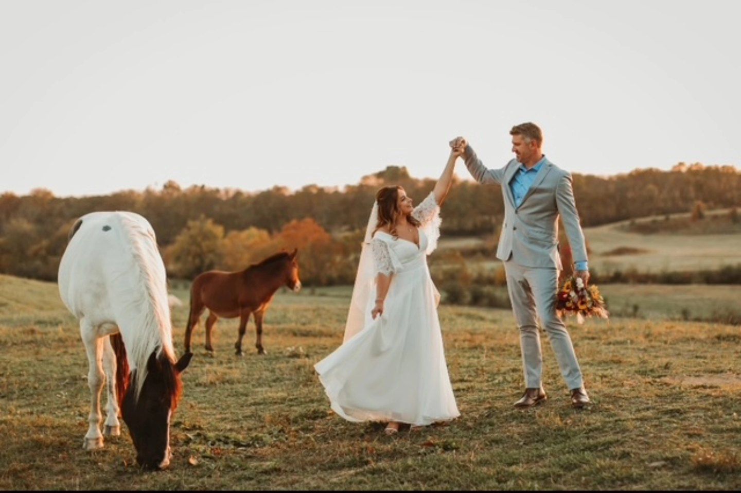 A bride and groom are dancing in a field with horses.