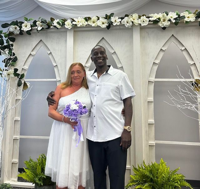 A bride and groom pose for a picture in front of flowers.