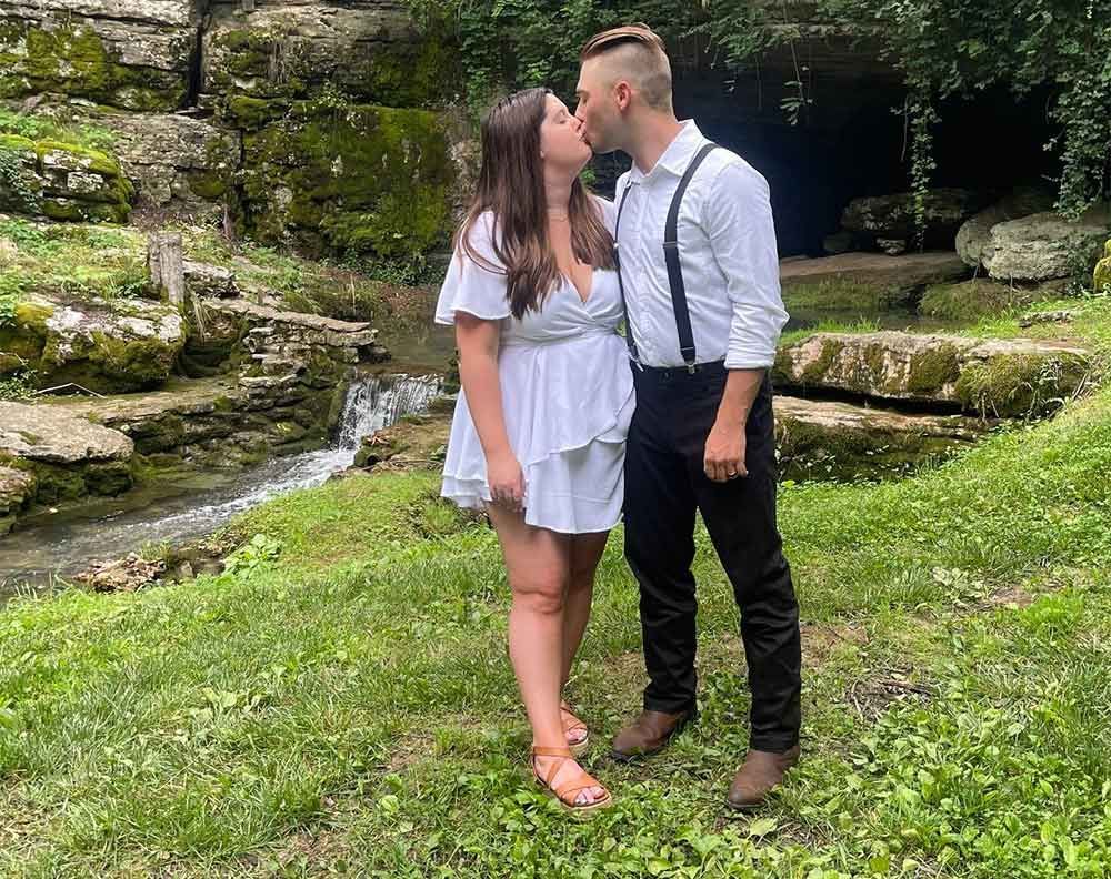 A man and a woman are kissing in front of a waterfall.
