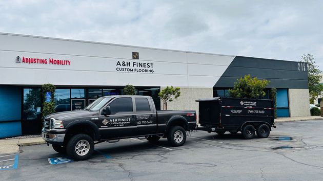 Black pickup truck towing a trailer outside a storefront with signage and large garage doors