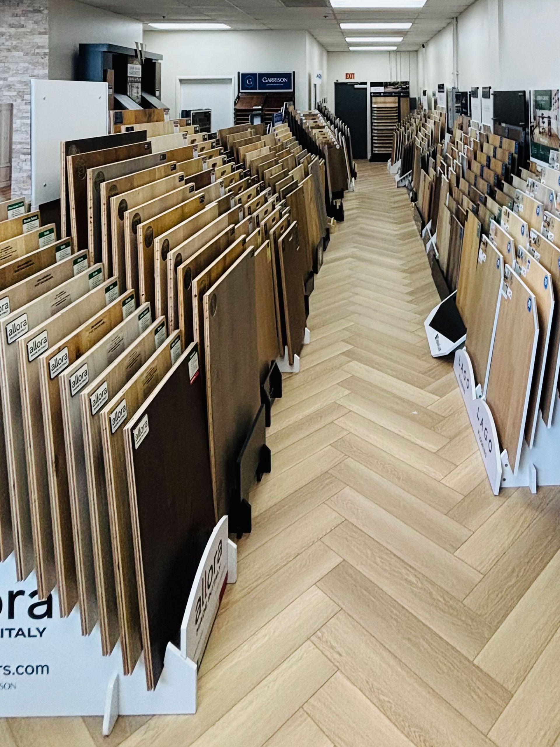 Rows of framed artwork displayed in a bright gallery room with a herringbone wood floor