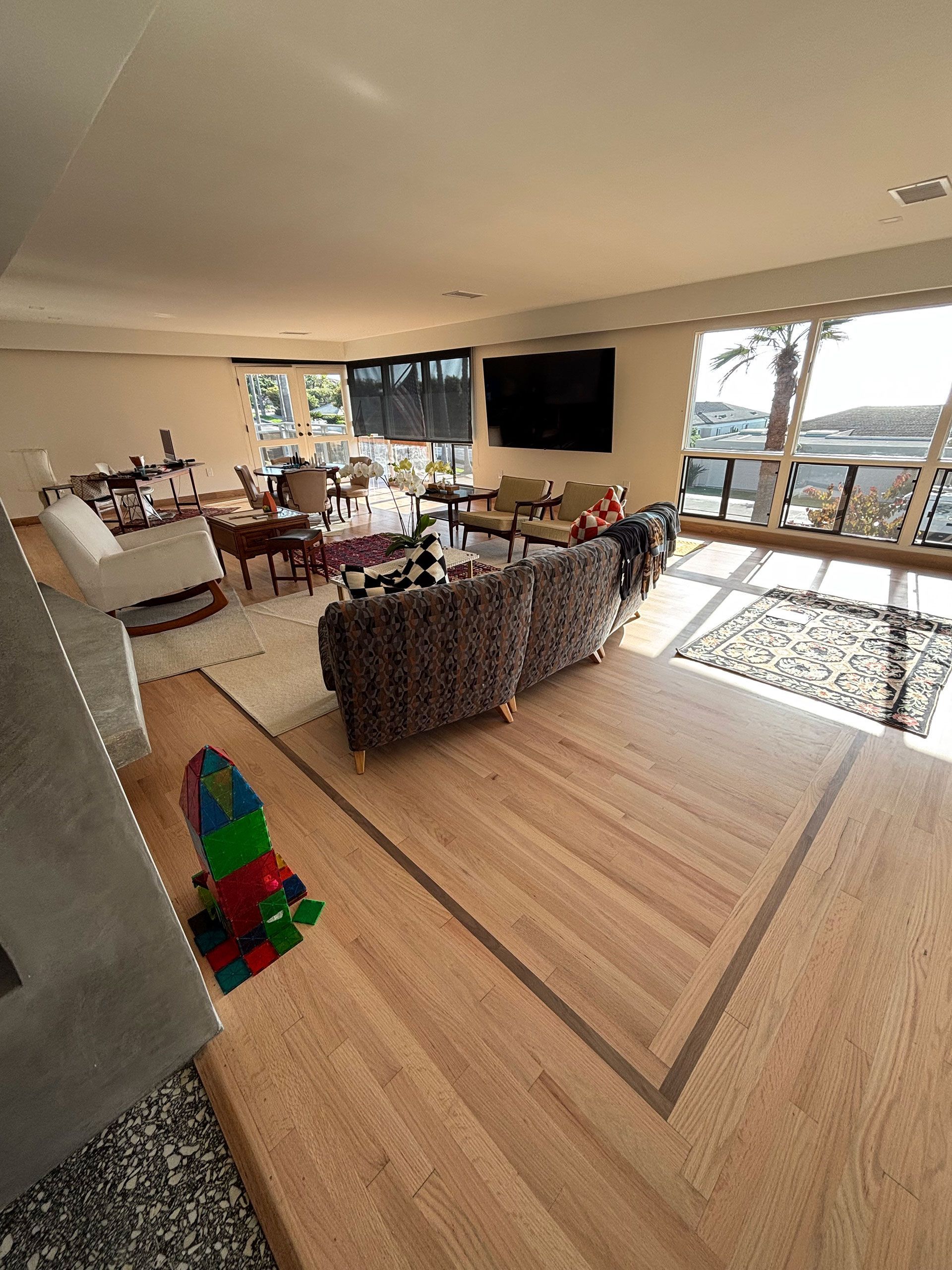 Modern living room with woven chairs, wall-mounted TV, large windows, and ocean view