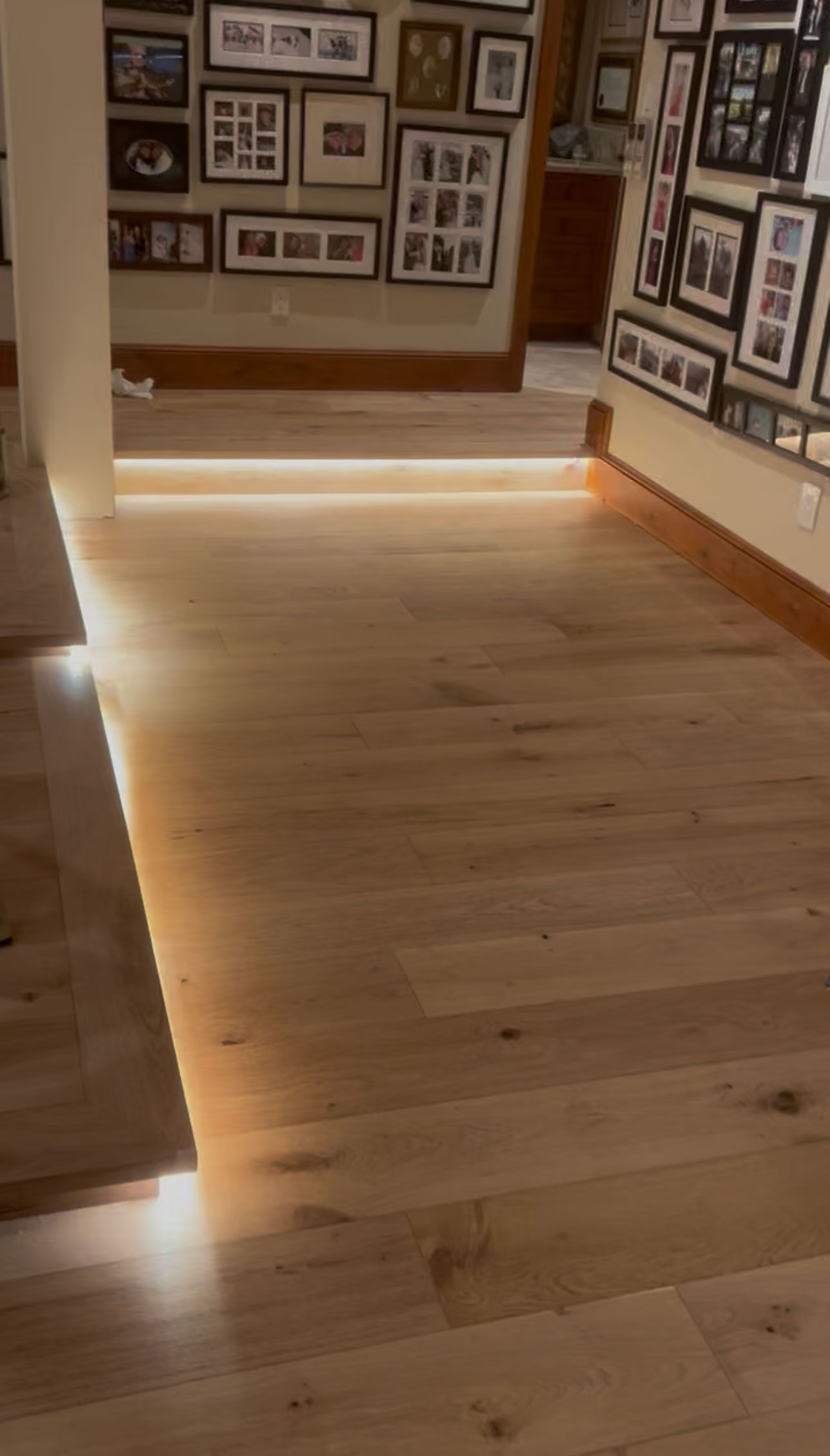 Wooden gallery hallway with framed photos on the walls and soft floor lighting.