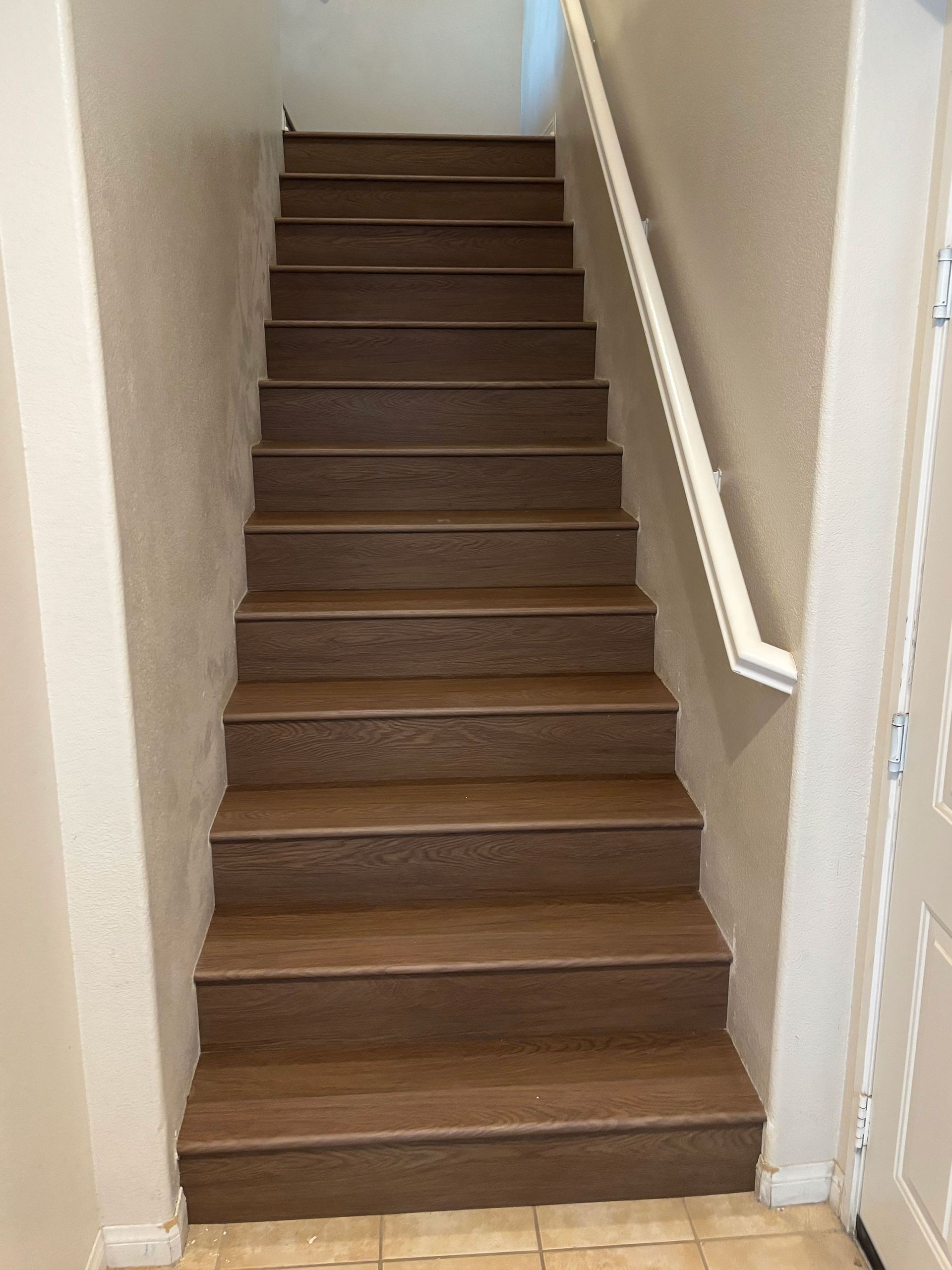 Narrow indoor staircase with brown carpeted steps and white walls