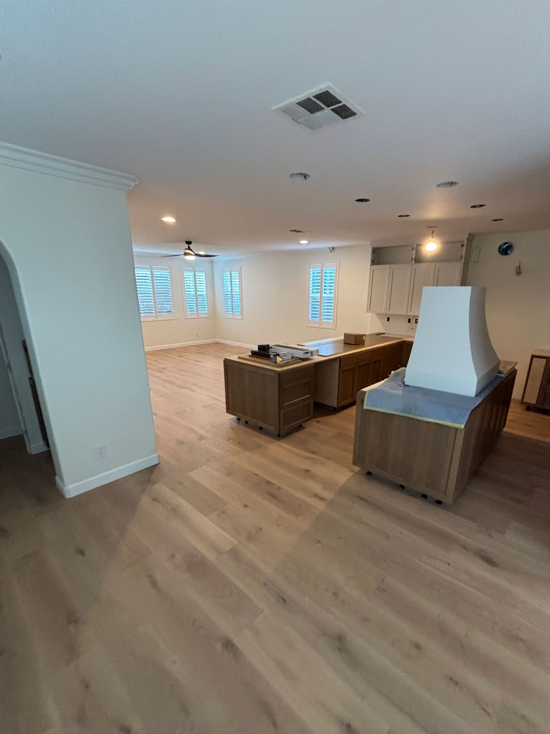 Empty modern living room with wood floors, white walls, island seating, and large windows