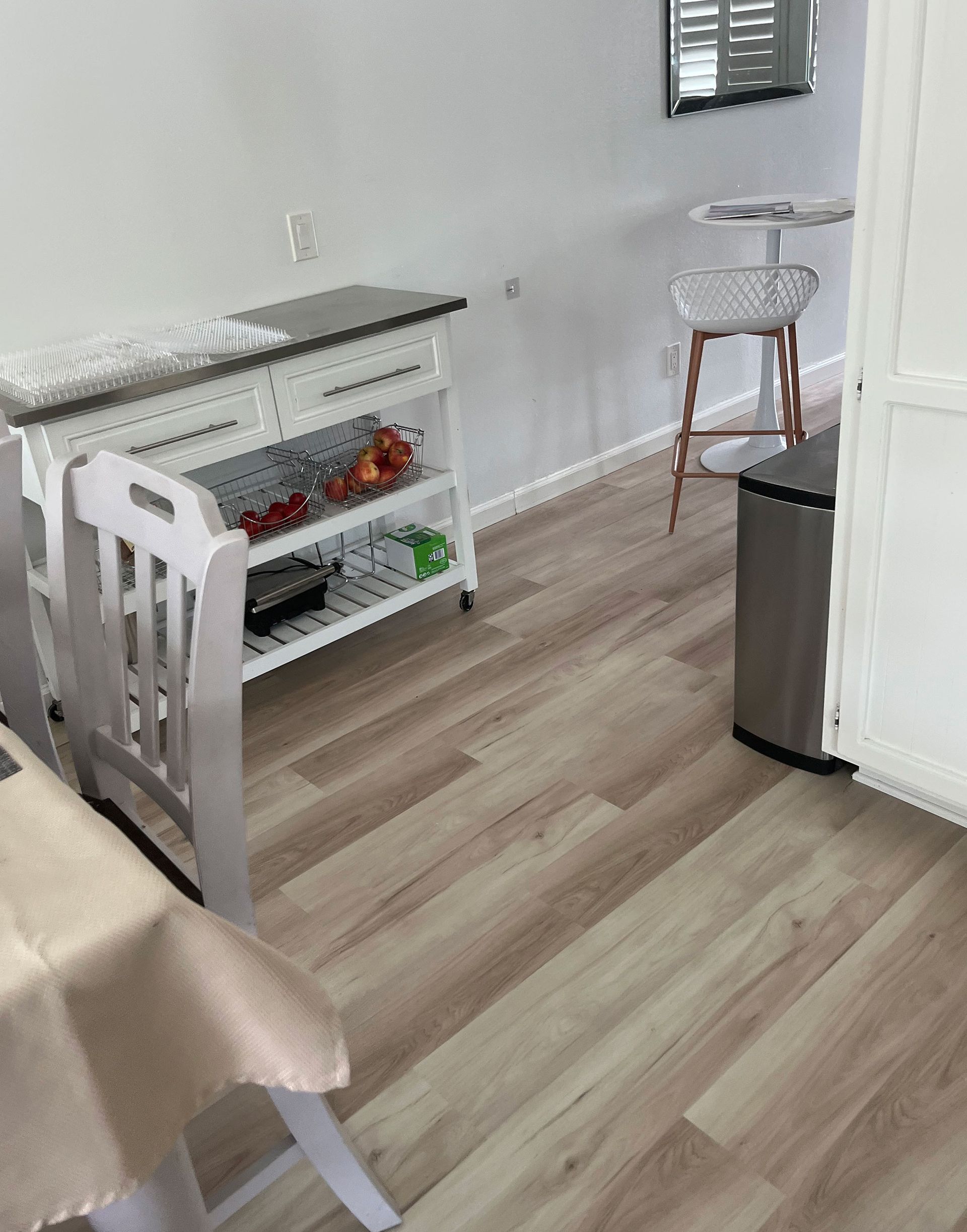 Small bright kitchen nook with white shelves, a stool, trash can, and wood-look flooring.