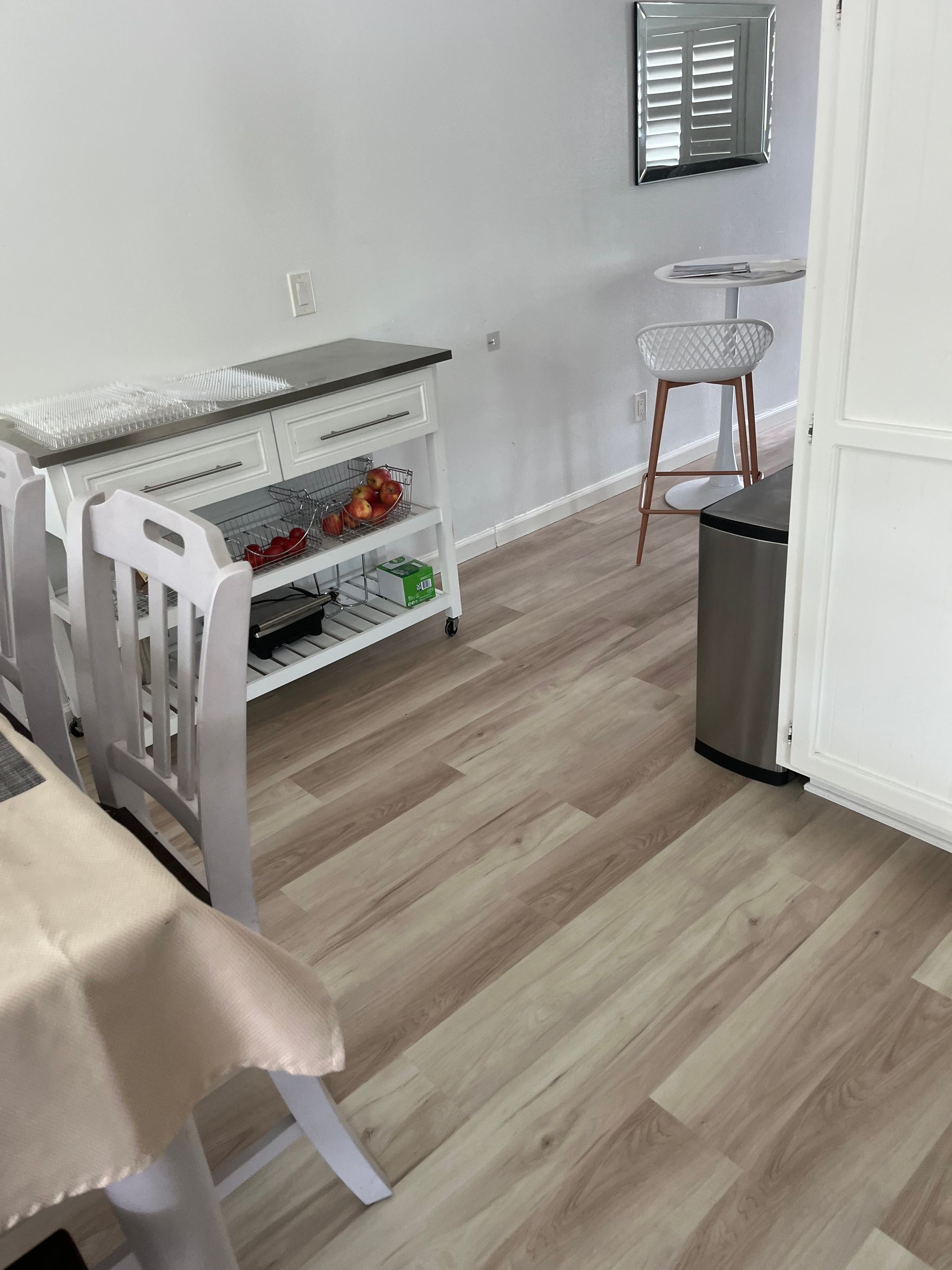 Bright kitchen with light wood floors, a white island, bar stool, and stainless trash can