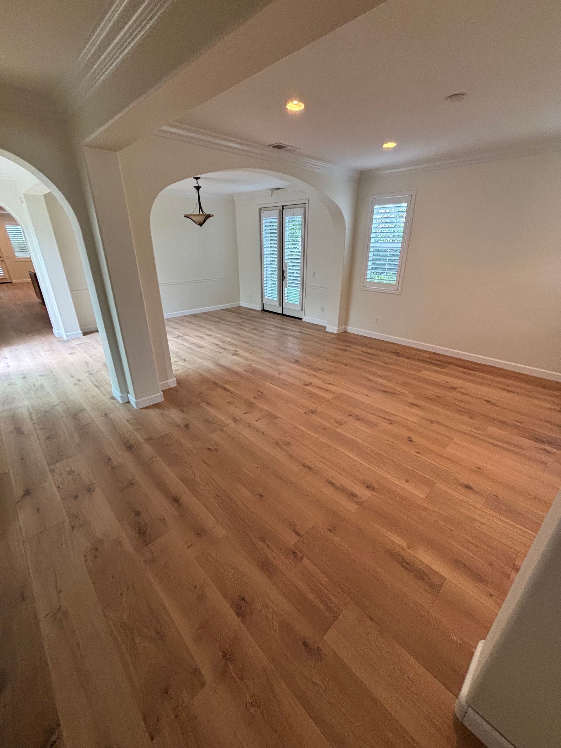 Empty room with hardwood floors, arched doorway, and white walls with windows and recessed lights