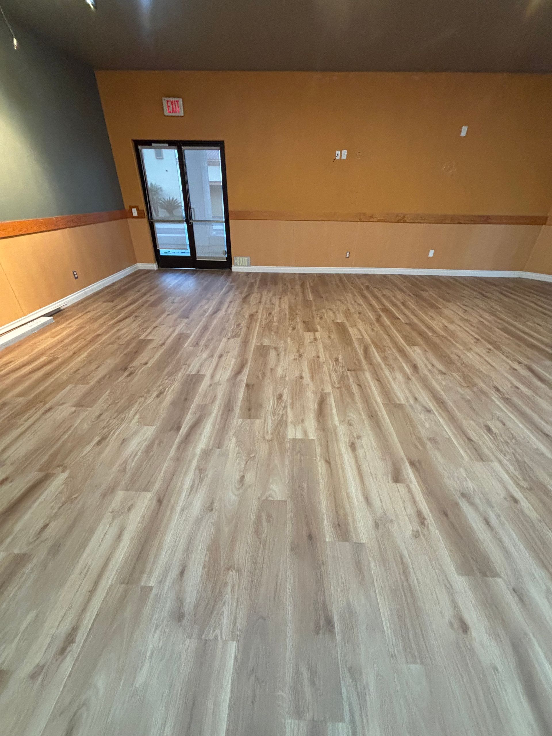 Empty room with wood flooring, tan walls, and a glass door at the back.