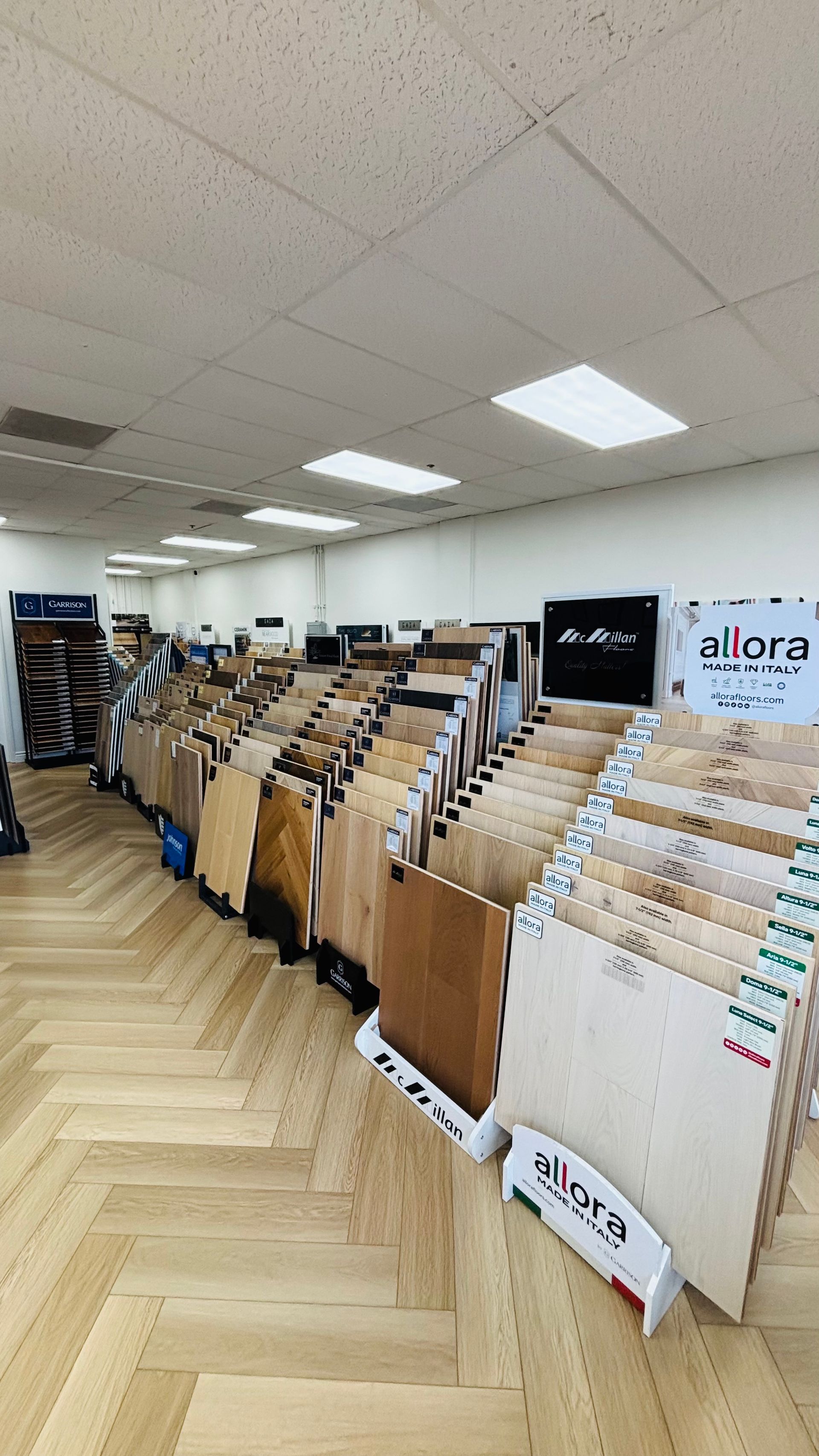 Rows of wood flooring samples displayed in a showroom with overhead lights and ceiling panels