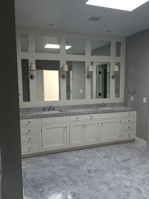 White vanity with gray marble countertop and mirrors, sconces, and drawers in a bathroom.
