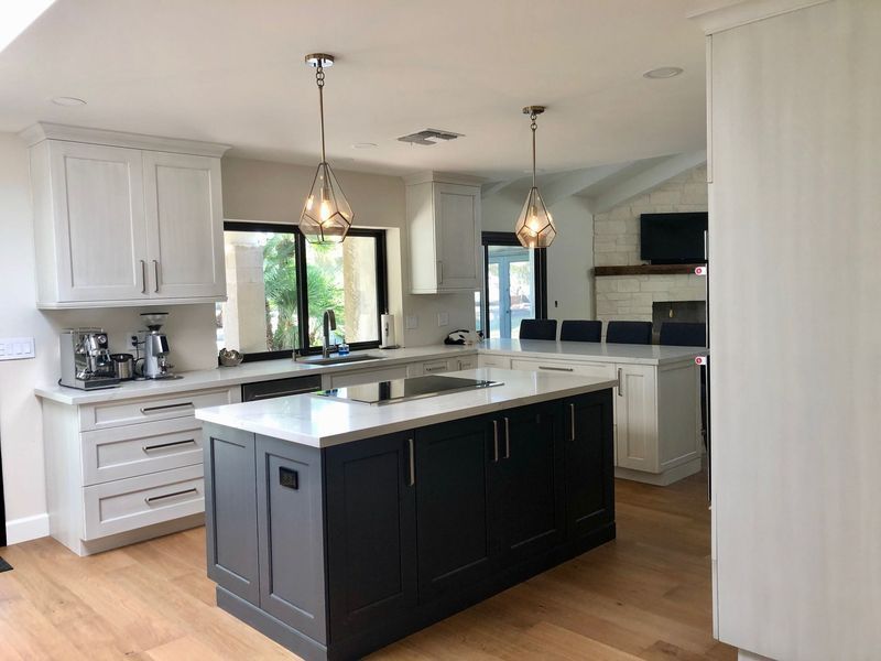 Modern kitchen with white and dark gray cabinets, island, hardwood floors, and pendant lights.