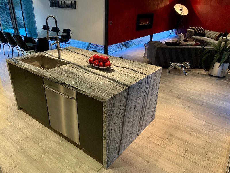 Modern kitchen island with sink, dishwasher, and granite countertop; tomatoes on top.