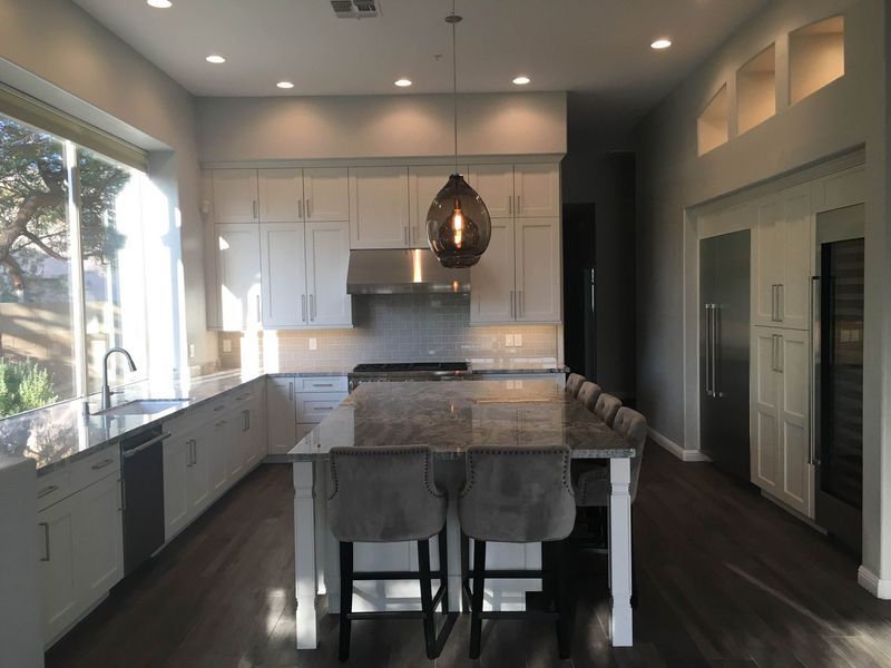 Bright kitchen with white cabinets, large island, stainless steel appliances, and a dark wood floor.