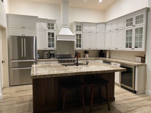 Kitchen with white cabinets, dark island, stainless steel appliances, and granite countertops.