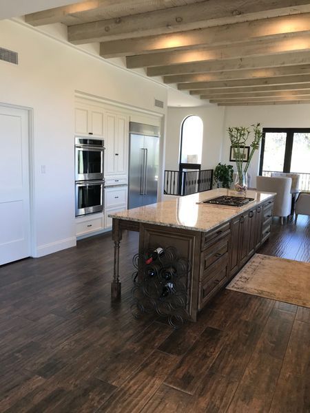 Elegant kitchen with island, wine rack, wood beams, stainless steel appliances, and dark wood floors.
