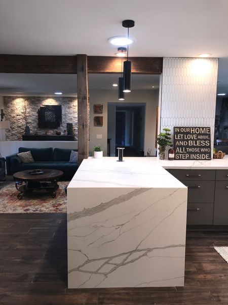 Modern kitchen with a marble-look island, wood floors, and a view into a living room with a fireplace and couch.