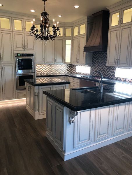Elegant white kitchen with black countertops, two islands, and chandelier.