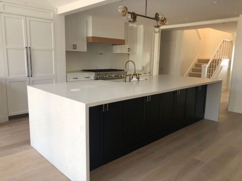 Modern kitchen with large white island, dark cabinets, stainless steel appliances, and wood floor.