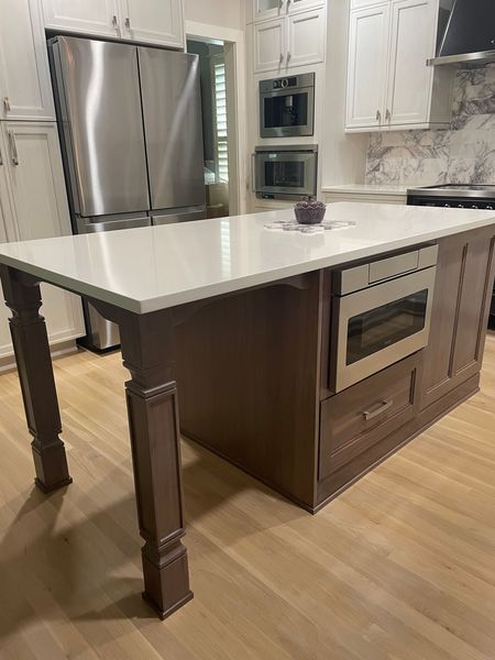 Kitchen island with a white countertop and brown cabinetry, including a microwave and drawer.