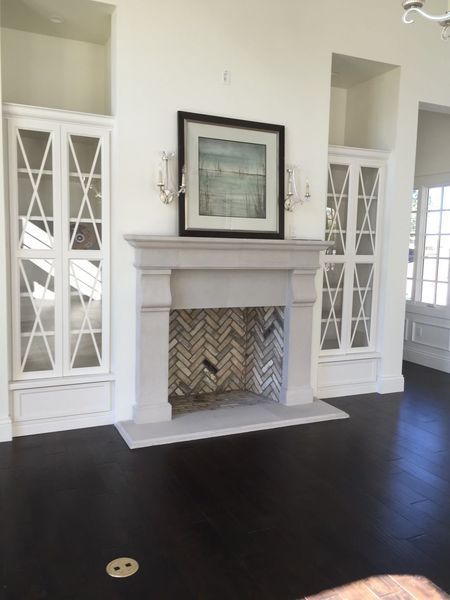 Fireplace with flanking white cabinets and a framed picture on a white wall. Dark floor.