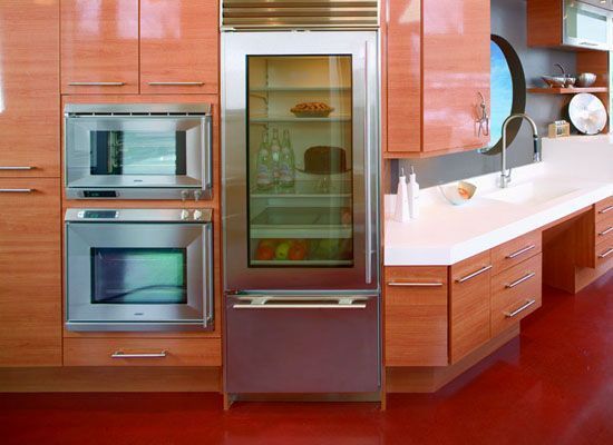 Modern kitchen with stainless steel appliances and glossy wood cabinetry; red flooring.