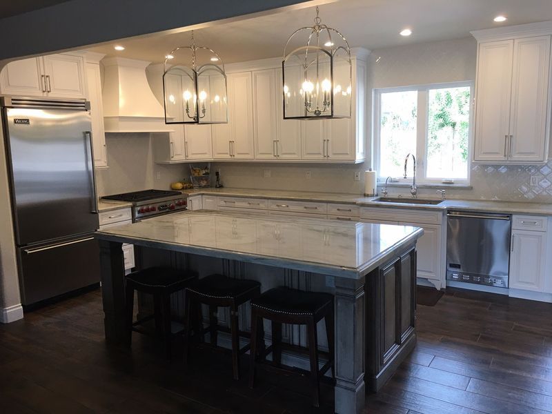 White kitchen with a large island, stainless steel appliances, and dark wood floors.