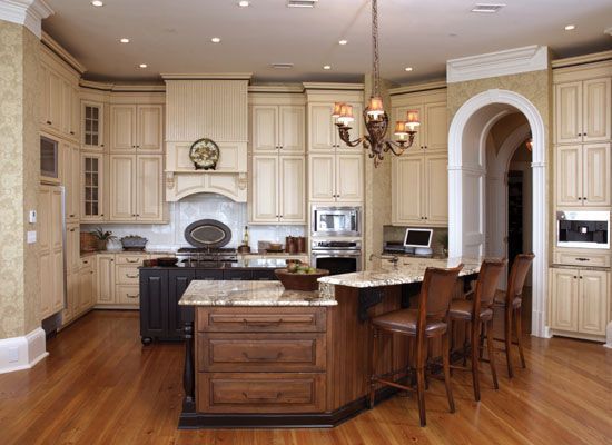 Elegant kitchen with light wood cabinets, dark island, and a chandelier.