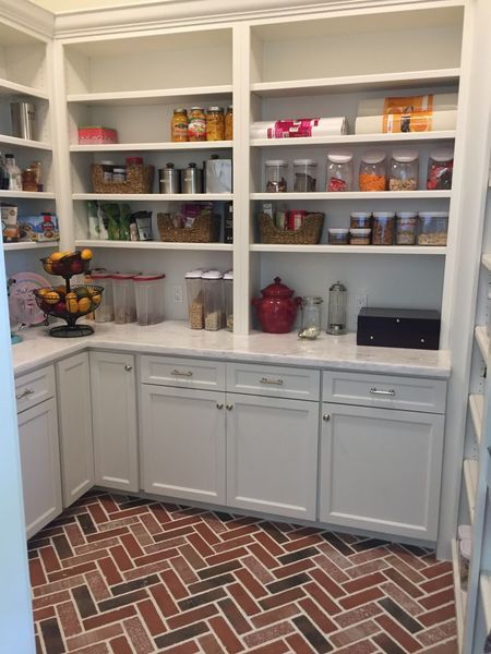 White pantry with brick floor, cabinets, and shelves stocked with food items.