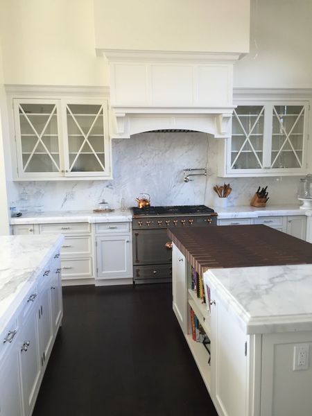 White kitchen with marble countertops, stainless steel range, and dark wood floors.