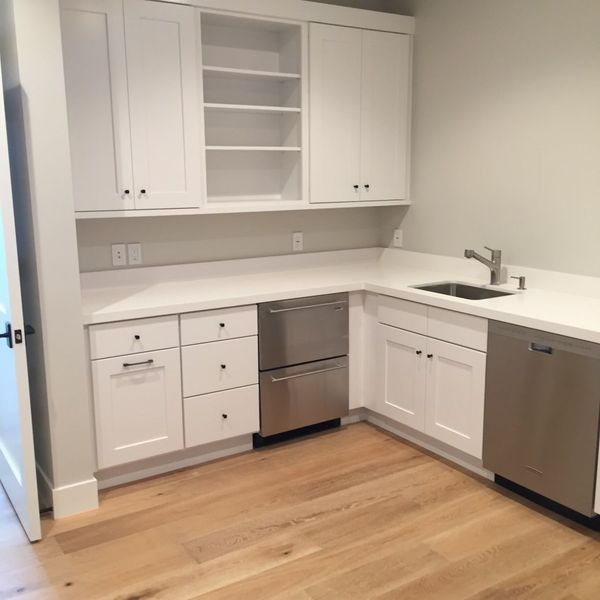 White kitchen cabinets with stainless steel appliances and a sink, next to hardwood flooring.