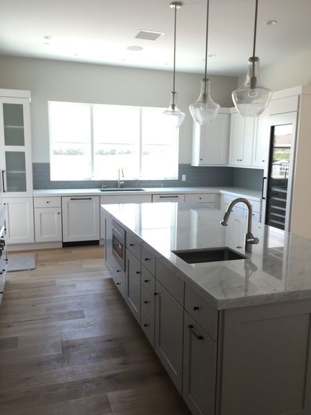 Bright white kitchen with large island, stainless steel faucet, and pendant lights.