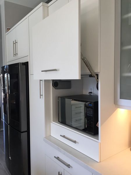 White kitchen cabinet with a hidden microwave. The cabinet door is open.