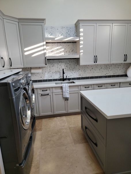 Laundry room with gray cabinets, white countertops, black faucet, and washing machine.