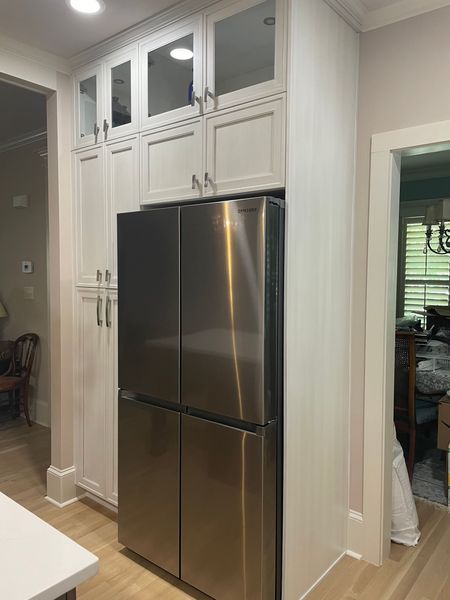 Stainless steel refrigerator flanked by white cabinets in a kitchen, with a doorway visible.