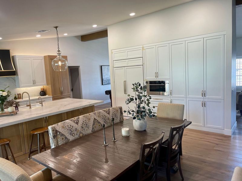 Dining room with a wooden table, white cabinets, and a kitchen island.