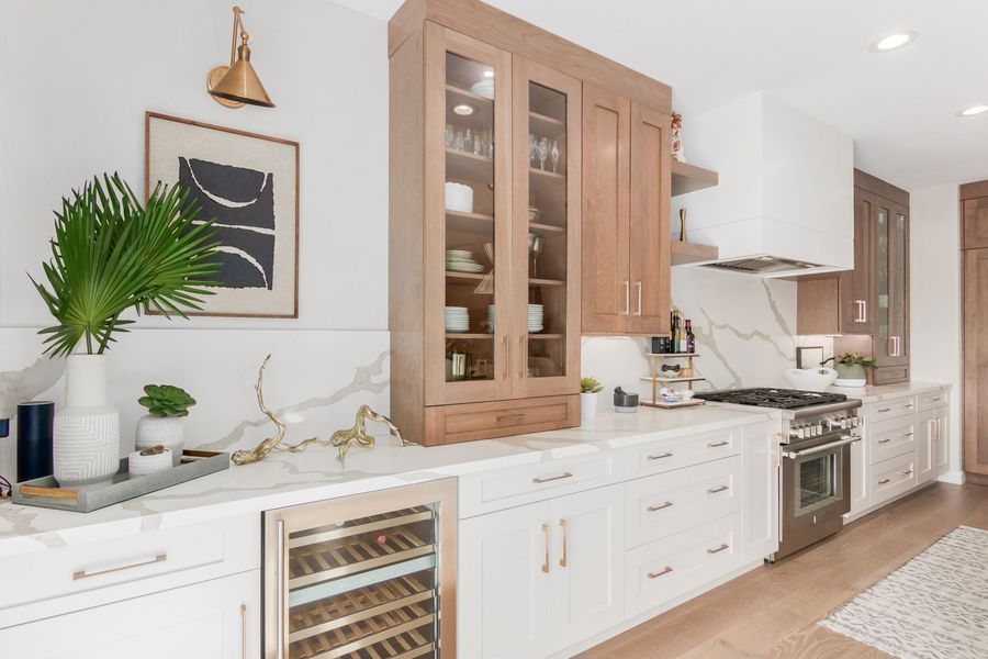 Modern kitchen with white cabinets, marble countertops, stainless steel appliances, and wood accents.