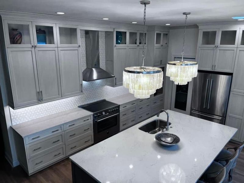 Modern kitchen with white cabinets, stainless steel appliances, and two chandelier lights.