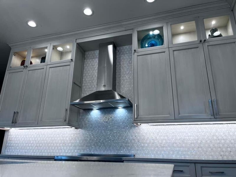 Kitchen with gray cabinets, stainless steel range hood, and white hexagon tile backsplash.