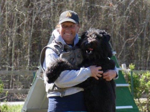 A man is holding a large black dog in his arms.