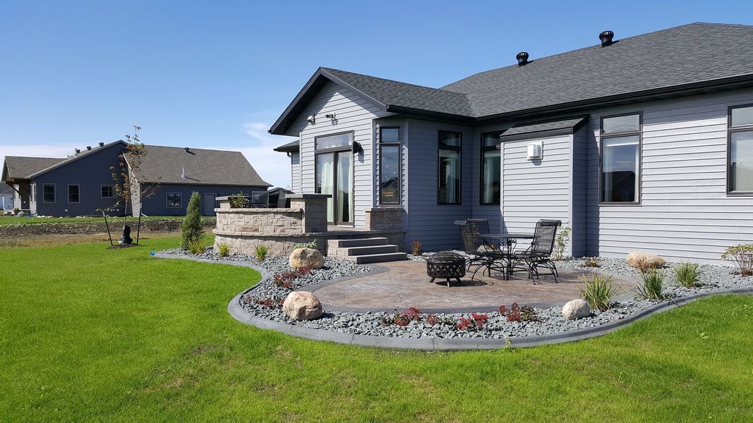 A modern gray house with a patio, lawn, and landscaping under a blue sky.