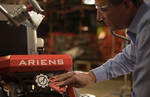 Man wiping an Ariens machine. Red machine with white logo, wearing safety glasses, industrial setting.