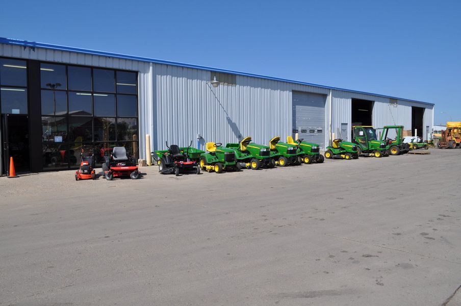 A dealership with John Deere lawn mowers and equipment outside; sunny day.