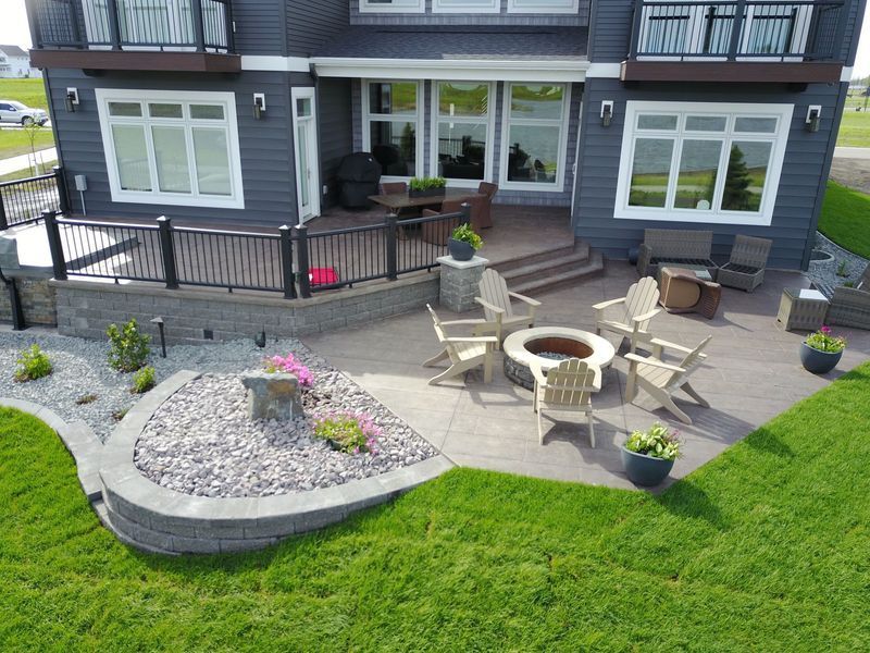 Backyard patio with fire pit, seating, retaining walls, and house with large windows.