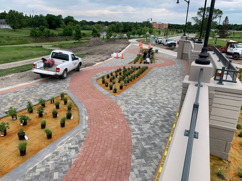 Construction site with brick pathways, workers planting, white truck, and landscaping.