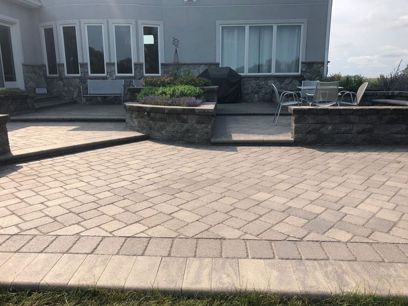 Stone patio with built-in seating, leading to a house with large windows.