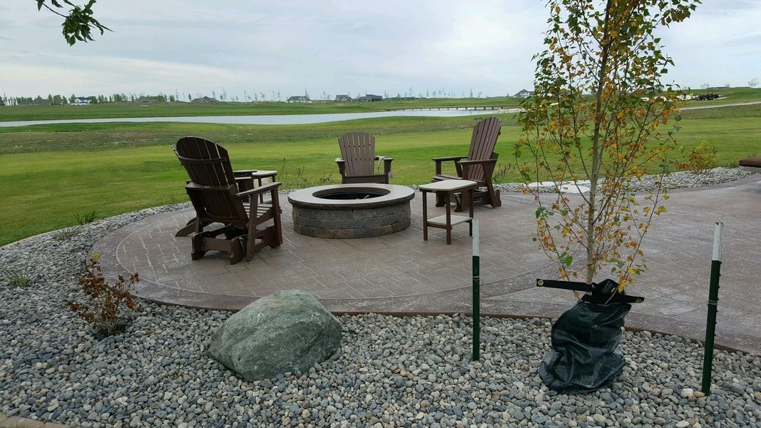 Outdoor seating area with fire pit, chairs, and surrounding gravel. Overcast sky and grassy landscape.