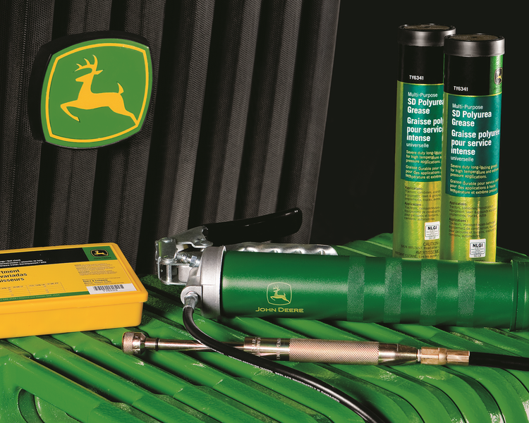 John Deere grease gun, cartridges, and accessories on green surface, with logo.