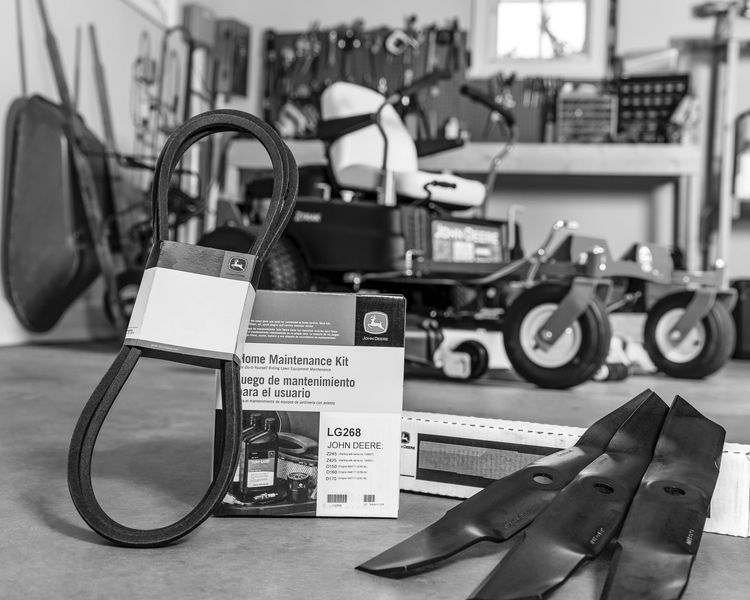 Lawnmower maintenance kit with blades and belt in front of a zero-turn mower in a garage.